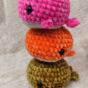 tres amigurumis con forma de ballena tejidas en lana de terciopelo suave. en color rosa, naranja y dorado